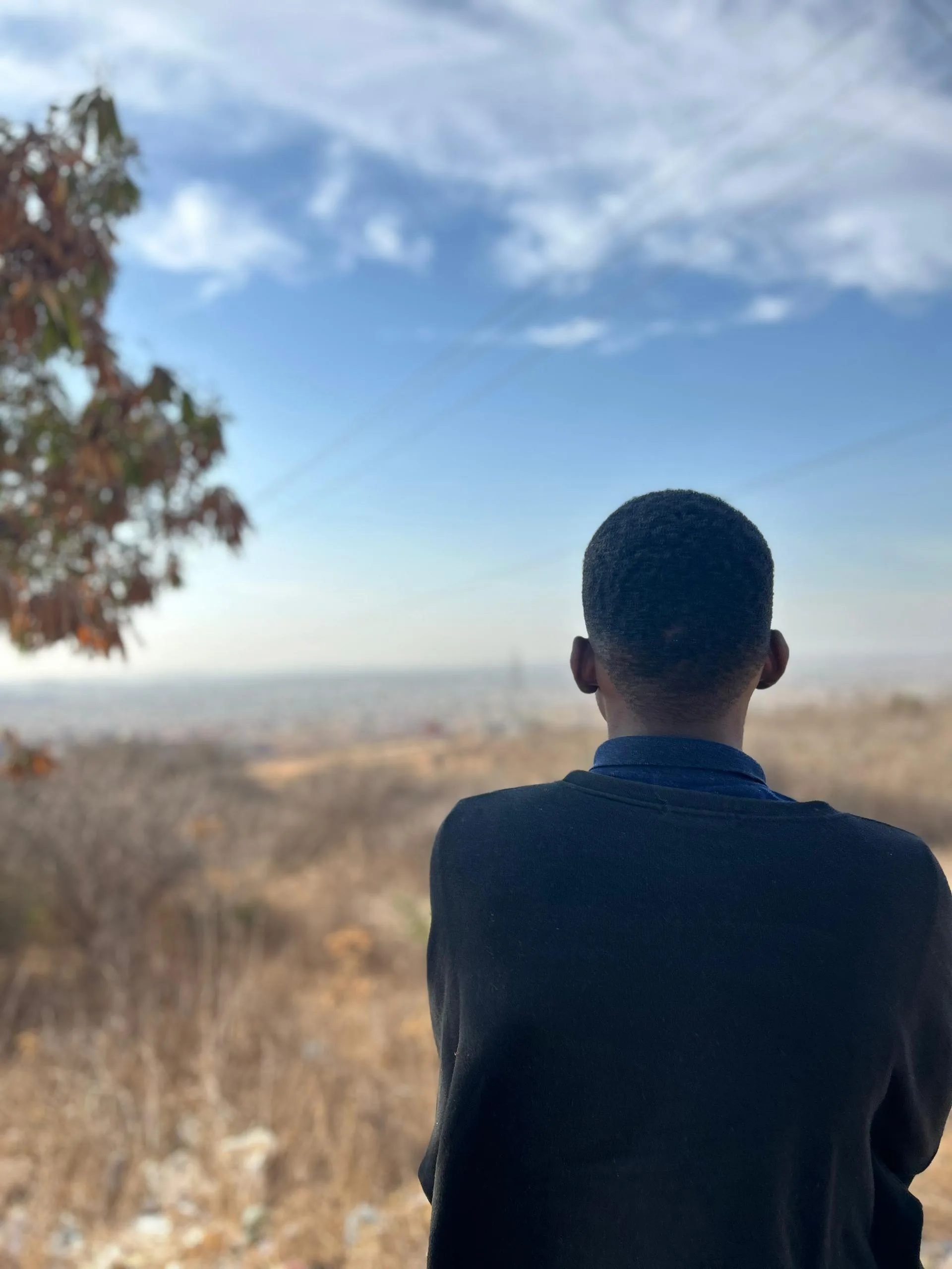 Harry Mbwasi seen from behind, looking out over a landscape.